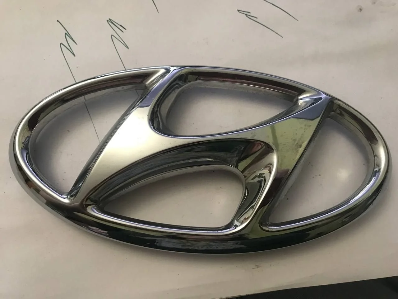 Эмблема решетки радиатора Hyundai Solaris 863594L500, передняя